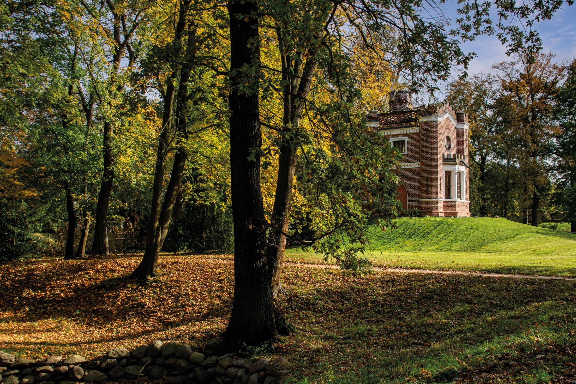 Maison de jardin en brique rouge de style néogothique sur une hauteur du Luisium, entourée d’arbres aux couleurs d’automne